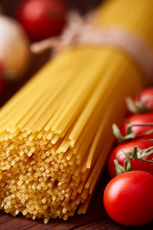 Uncooked pasta, tomatoes and two spoons on wooden background, top view, close-up, selective focusの写真素材