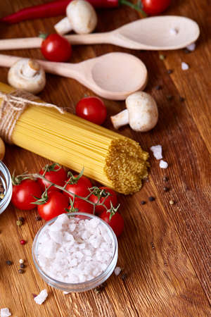 Uncooked pasta, tomatoes and two spoons on wooden background, top view, close-up, selective focusの写真素材