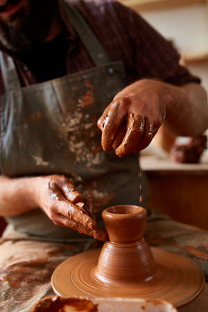 Close-up hands of a male potter in apron making a vase from clay, selective focusの写真素材