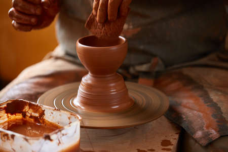 Close-up hands of a male potter in apron molds bowl from clay, selective focus