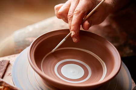 A potter paints a clay plate in a white in the workshop, top view, close-up, selective focus.