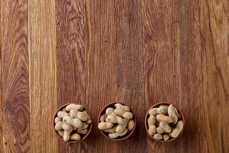 Unpeeled peanuts in wooden bowl over rustic wooden background closeup, selective focus. Some copy space for your text. Healthful and nutritious snack. Delicious ingredient for your every day cooking. Healthy lifestyle concept.の写真素材