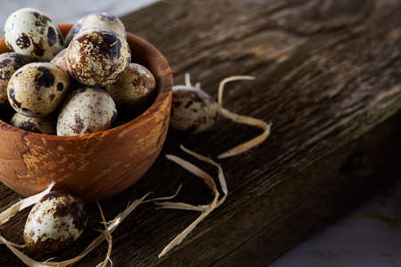 Wooden bowl filled with quail eggs on wooden board over white background, close-up, selective focus.の写真素材