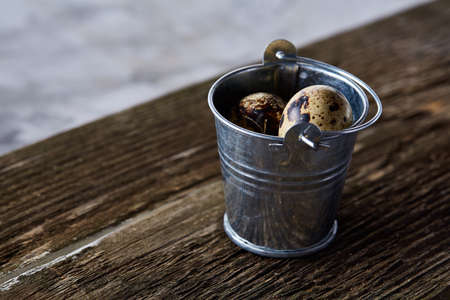 Small decorative bucket filled with quail eggs on wooden board over white background, close-up, selective focus.の写真素材