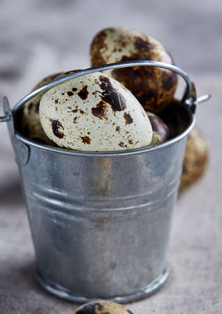 Small decorative bucket filled with quail eggs on napkin over white textured background, close-up, selective focus.の写真素材