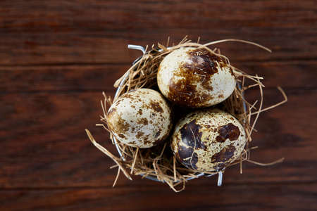 Three quail eggs in hay nest over dark wooden background, close up, selective focus