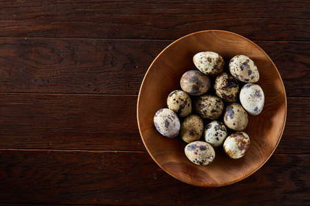 Fresh quail eggs in a wooden plate on a dark wooden background, top view, close-upの写真素材