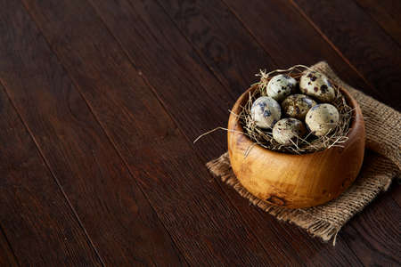 Fresh quail eggs in a wooden bowl on a homespun napkin over dark wooden background, top view, close-upの写真素材