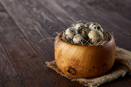 Fresh quail eggs in a wooden bowl on a homespun napkin over dark wooden background, top view, close-upの写真素材