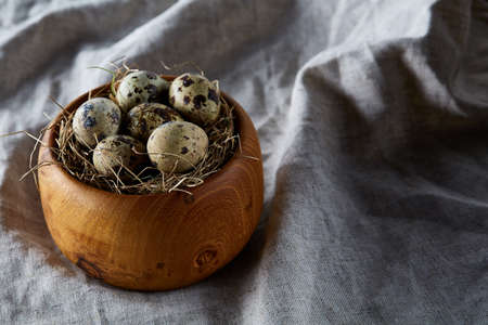 Quail eggs in a wooden bowl on a homespun tablecloth, top view, close-upの写真素材