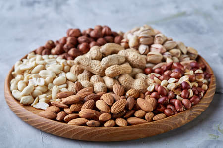 Mixed nuts in brown bowls on wooden tray over white background, close-up, top view, selective focus.の写真素材