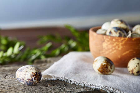 Wooden bowl with quail eggs, eggs on a homespun napkin on piece of board and boxwood branches over...