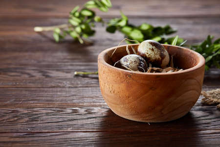 Wooden bowl with quail eggs, eggs on a homespun napkin on piece of board and boxwood branches over wooden background, close-up, selective focus. Conceptual Easter still life. Decorative rural composition. Healthy eating. Healthy food concept.の写真素材