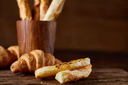 Puff pastries on piece of board over dark wooden table, close-up, selective focus, backlight.