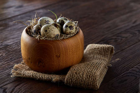 Rustic still life with quail eggs in bucket, box and bowl on a linen napkin over wooden background,...