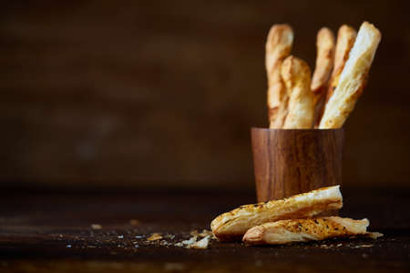 Delicious breadsticks grissini on wooden dark background in wooden oldstyle cup, close-up, selective...