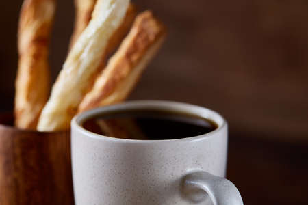 Coffee cup, breadsticks and croissants on an old wooden background, close-up, selective focus.
