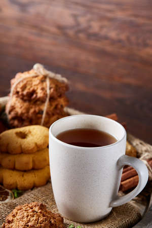 White porcelain cup of hot tea, cookies and spicies on a wooden barrel, selective focus, close-up, vertical.の写真素材