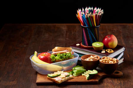 Concept of school lunch break with healthy lunch box and school supplies on wooden desk, selective focus.の写真素材