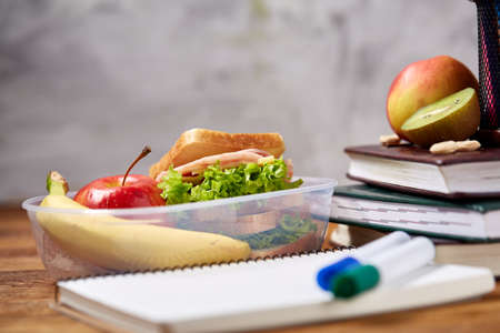 Concept of school lunch break with healthy lunch box and school supplies on wooden desk, selective focus.の写真素材