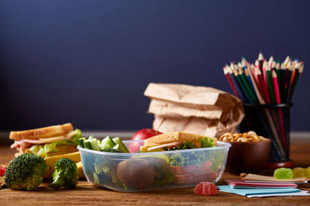 Back to School concept, school supplies, biscuits, packed lunch and lunchbox on white desk, selective focus, close-up.の写真素材
