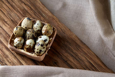 Spotted quail eggs arranged in rows in a box on a rustic wooden background, top view, selective...