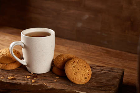 White porcelain mug of black tea or earl grey and pile of sweet cookies on flat piece of wood over rustic wooden background, top view, selective focus. Studio shot. Morning concept. Healthy eating concept.の写真素材