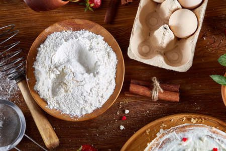 Top view raw ingredients for cooking strawberry pie or cake on wooden table: eggs, flour, milk,...