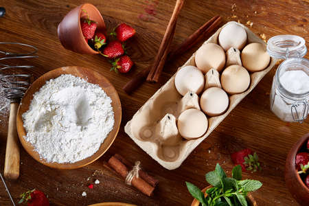 Top view raw ingredients for cooking strawberry pie or cake on wooden table: eggs, flour, milk, sugar and strawberry, flat lay. Bakery background. Recipe for strawberry pie. Tasty morning pastry. Homemade food concept.の写真素材