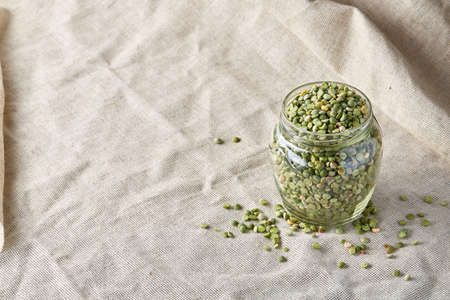 Raw green peas in glass jar on homespun tablecloth, close-up, selective focus. Some copy space for your inscription. Organic protein. Perfect ingredient for vegan cuisine. Healthy food concept. Healthy eating, dieting.の写真素材