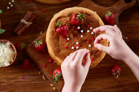 Close up of girl's hands decorating top of delicious strawberry cake, close up, selective focus....