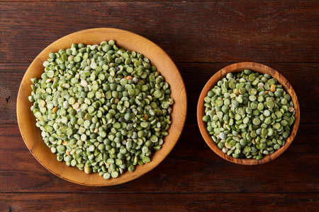 Nutritious green peas in a bowl and in a plate on rustic wooden background, close-up, top view,...