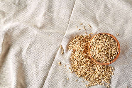 Oat groats or oat spike in wooden plate on homespun tablecloth background, copy space, top view, selective focus. Healthy eating, dieting. Natural nutritious oatmeal. Vegan cuisine. Organic food concept.の写真素材