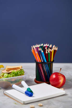 Back to School concept, school supplies, assortment of biscuits, paper paper with food and transparent lunchbox full of sandwich, fruits and vegetables together with assortment of biscuits over white chalkboard, selective focus, close-up.の写真素材