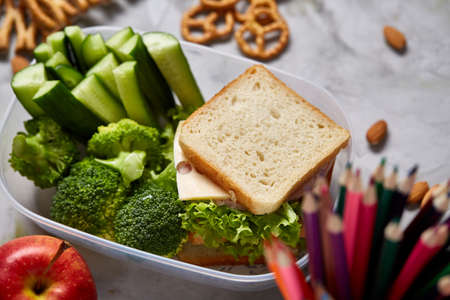school supplies, assortment of biscuits, paper paper with food and transparent lunchbox full of sandwich, fruits and vegetables together with assortment of biscuits over white chalkboard, selective focus, close-up.の写真素材