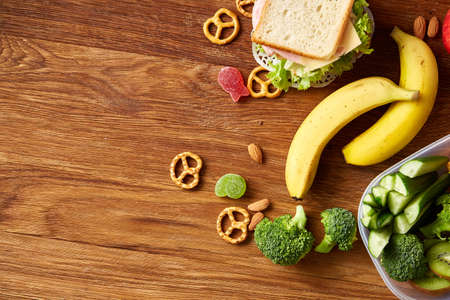 Preparing ham and cheese sandwiches for school lunchbox on wooden background, close up. Healthy eating habits concept. Dietary composition with sandwiches, biscuits and lettuce on rustic wooden background. Preparation for having a snack.の写真素材