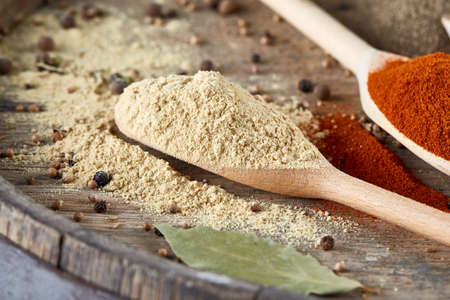 Top view of a wooden spoons full of paprica and curry with a bay leaf on wooden barrel background,...