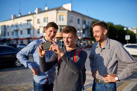 Portrait of a group of smiling friends, preparing for making selfie on camera on urban background.