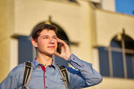 A handsome teen is taling on his phone while walking around the city on the background of the building.の写真素材