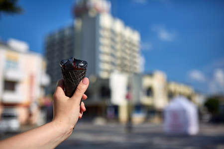 A first person view, girl walking along the road, holding ice cream in her hands and eating it in front of the modern building background, shallow depth of field. Yummy chocolate ice-cream. Sweet refreshing summer food concept.の写真素材
