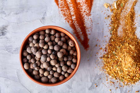 Allspice in ceramic bowl among ground scattered spicies on white textured background close-up, top view, selective focus. Exotic asian spice. Aromatic condiment. Healthy eating and dieting concept.の写真素材