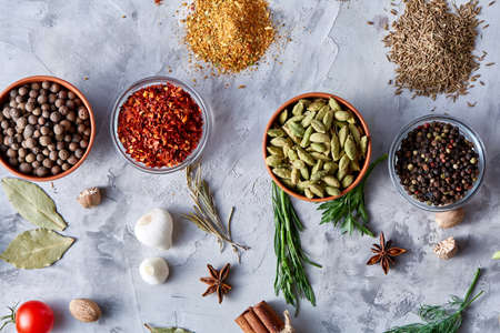 Clay bowls with spices arranged in rows with other herbs on white textured background, view from above, selective focus. Bowls with chilly, peppercorns, cardamon togather with anise star, bay leaf, parsley, nutmeg, dill, rosemary.の写真素材