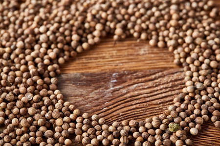 Circle frame made of coriander seeds on the rustic wooden background, close-up, top view, macro, selective focus. Some copy space for your inscription. Natural antioxidant. Organic condiment. Exotic flavoring. Healthy food concept.の写真素材