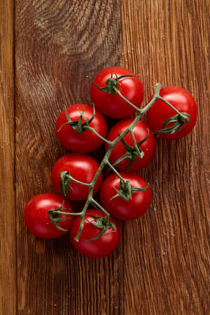A bunch of fresh cherry tomatoes on rustic wooden background, top view, selective focus, vertical. Healthy organic vegetables. Eco heap. Healthy eating and dieting concept. Cooking and gastronomy concept.の写真素材