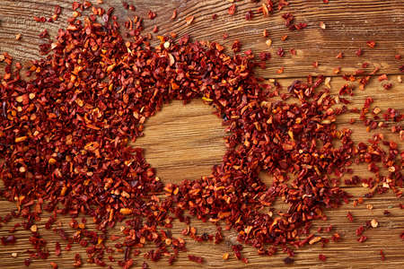 Abstract pattern of dried red hot chilly flakes on rustic wooden background, top view, close-up,...