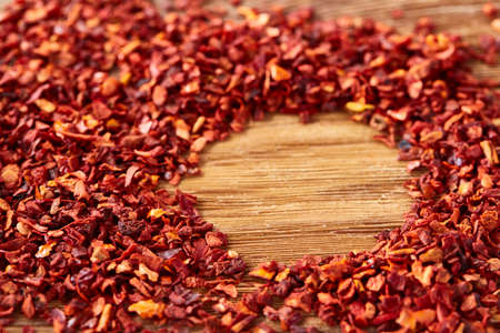 Circle framing made of dried red hot chilly flakes on rustic wooden background, top view, close-up,...