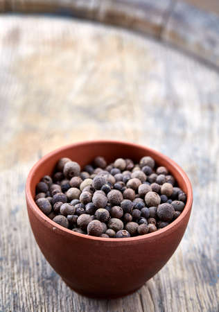 Clay bowl with dried allspice berries on wooden barrel, top view, close-up, macro, selective focus, vertical. Some copy space for your text. Exotic asian spice. Piquant flavour. Aromatic condiment. Healthy eating and dieting concept.の写真素材