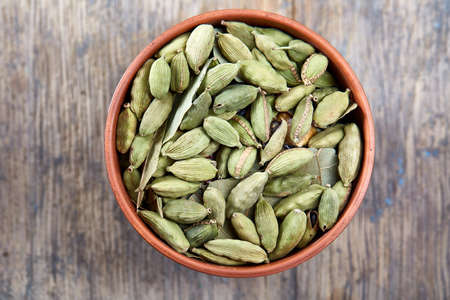 Green cardamon in ceramic bowl on vintage wooden background close-up, top view, selective focus. Some copy space for your text. Exotic indian spice. Aromatic condiment. Healthy eating and dieting concept.の写真素材