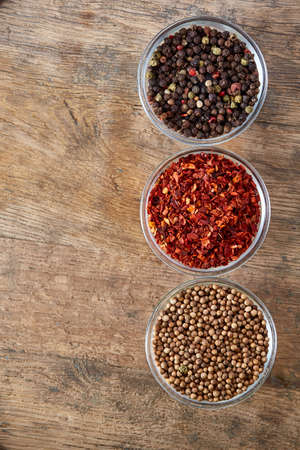 Three bowls with assortment of spicy arranged in row on wooden table, top view, close-up, selective focus, vertical. Peppercorn, chilly, coriander on vintage wooden background. Aromatic flavouring. Healthy eating and dieting concept.の写真素材