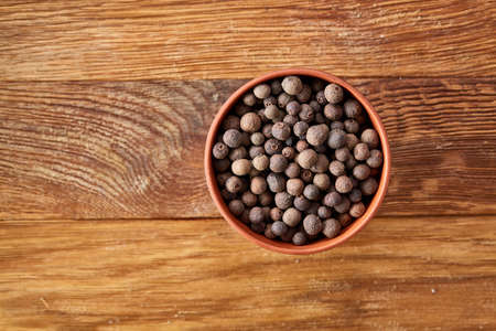 Clay bowl with dried allspice berries on vintage wooden background, top view, close-up, macro, selective focus. Some copy space for your text. Exotic asian spice. Piquant flavour. Aromatic condiment. Healthy eating and dieting concept.の写真素材